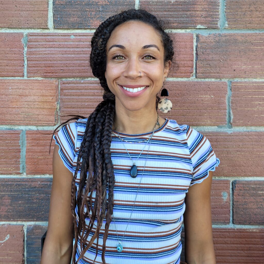 A woman with long dreadlocks standing in front of a brick wall.