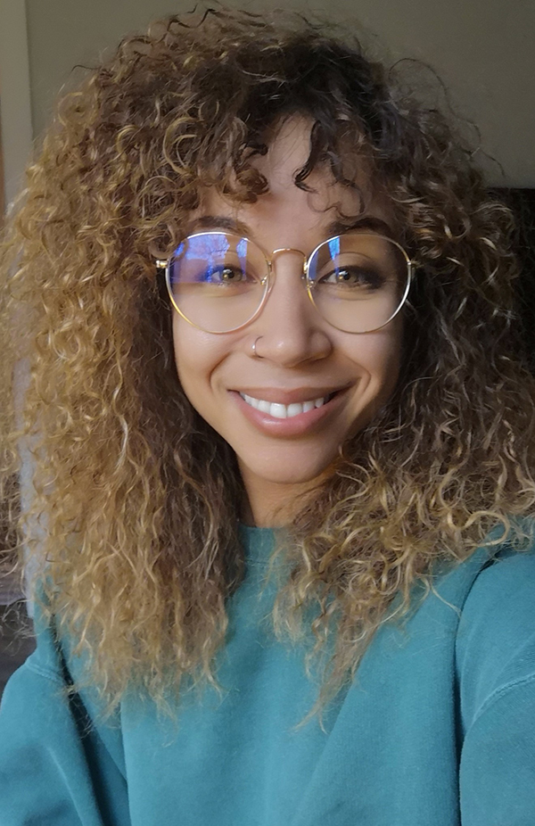 A woman with curly hair and glasses smiling for the camera.